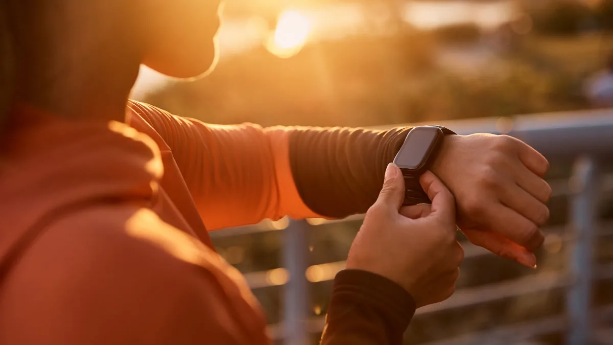 Person checking their smartwatch at sunset on a bridge